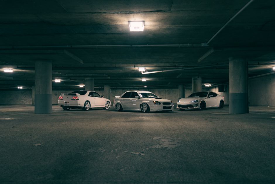 Three sleek cars parked in a dimly lit urban indoor garage, highlighting modern automotive design.